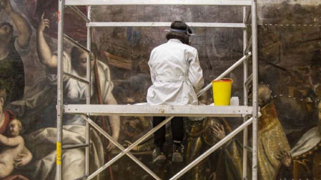 restauratrice su impalcatura di fronte a un dipinto