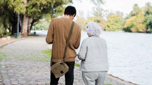 Bando Assistenza Anziani Due persone di schiena passeggiano all'aperto, sono un uomo giovane e una donna anziana