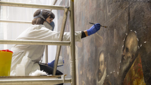 restauratrice con camice e maschera protettiva nell'atto di restaurare un quadro 