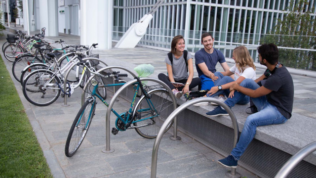 Quattro ragazzi, di cui due femmine e due maschi, seduti una panchina a chiacchierare e accanto a loro le biciclette