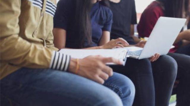 dettaglio di persone sedute mentre scrivono al pc e compilano moduli cartacei