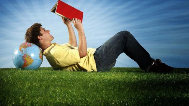 Un uomo legge un libro in un prato con la testa appoggiata al mappamondo