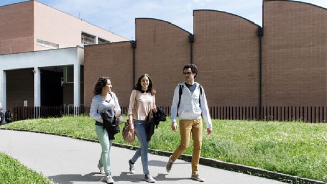 Due studentesse e uno studente che camminano lungo il viale all'interno di un campus universitario