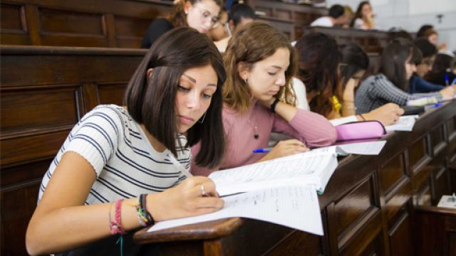 Studentesse sedute in aula di lezione, con una studentessa in primo piano che prende appunti