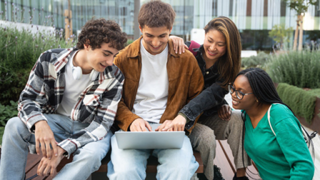 Studenti e studentesse Quattro studenti sorridenti, due ragazzi e due ragazze, sono seduti in uno all'aperto, guardano un pc portatile