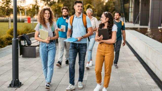Studenti e studentesse Studenti sorridenti che camminano con libri in mano e zaini sulle spalle