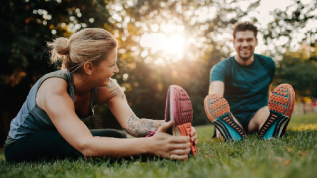 foto di due sportivi, un ragazzo e una ragazza che fanno stretching su un prato