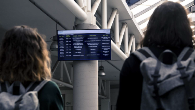 Immagine di due studentesse con zaini sulle spalle che guardano un monitor che contiene indicazioni sulle lezioni