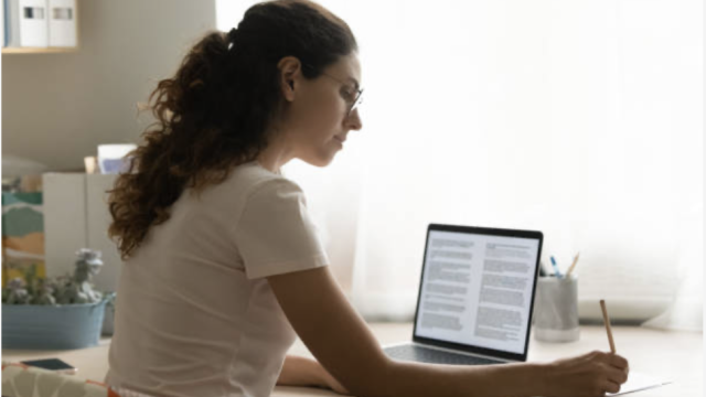 Ragazza alla scrivania scrive su carta guardando un testo al pc