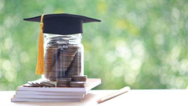 contenitore di vetro pieno di monete, appoggiato su una pila di libri e coperto da un tocco di laurea
