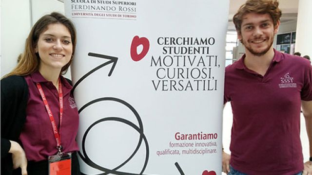 Un ragazzo e una ragazza sorridono di fianco al totem della Scuola Ferdinando rossi