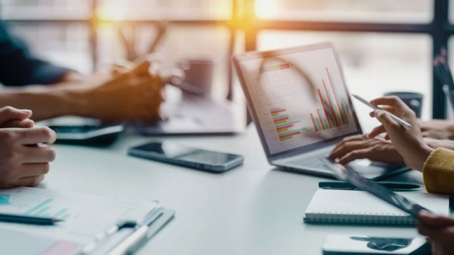 Studenti che studiano seduti intorno ad un tavolo con la presenza di computer, cellulari, blocchetti per appunti