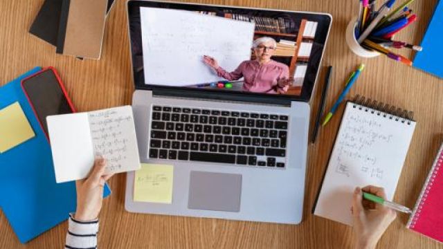 Studentessa segue lezione a distanza con computer sulla scrivania e blocco appunti