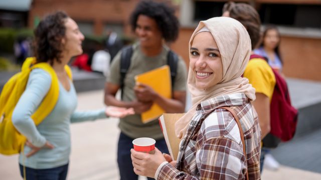 ragazza sorride alla fotocamera. Sullo sfondo un gruppo di studenti