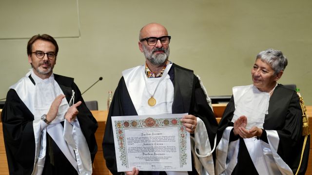 Due uomini sulla sinistra e una donna sulla destra che indossano la toga. L'uomo al centro ha in mano una pergamena