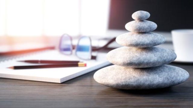 sassi impilati su di una scrivania, un quaderno, due matite e un paio di occhiali