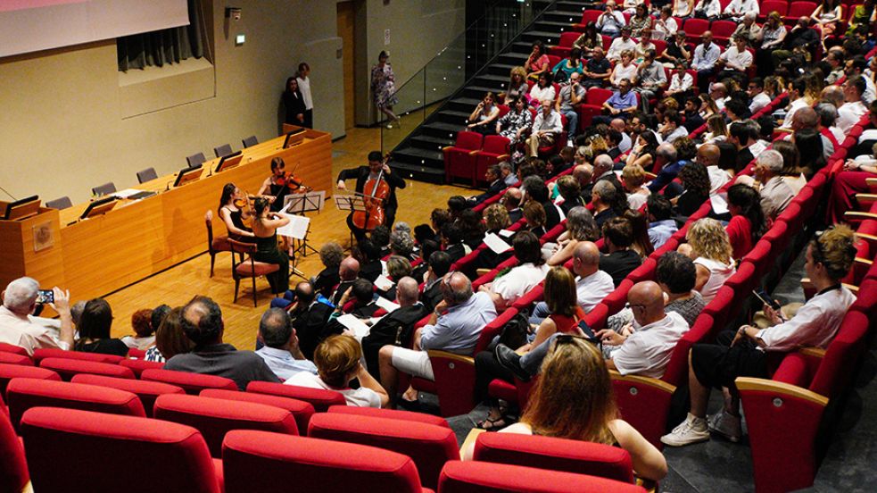Quatto persone suonano il violino di fronte al pubblico della Festa della Conoscenza Migliori Laureate e Laureati nell'aula magna della Cavallerizza