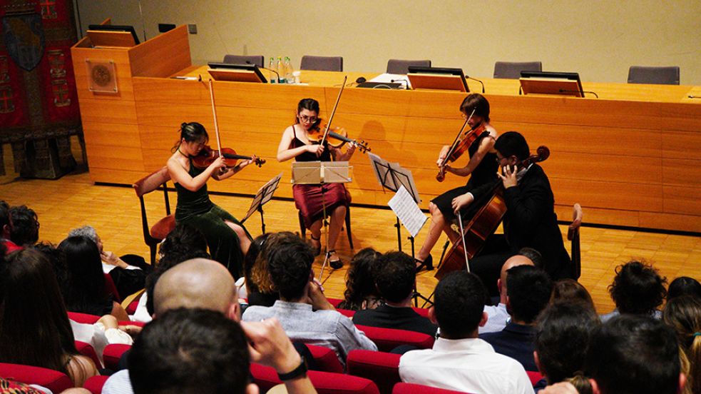 Quatto persone suonano il violino di fronte al pubblico della Festa della Conoscenza Migliori Laureate e Laureati nell'aula magna della Cavallerizza