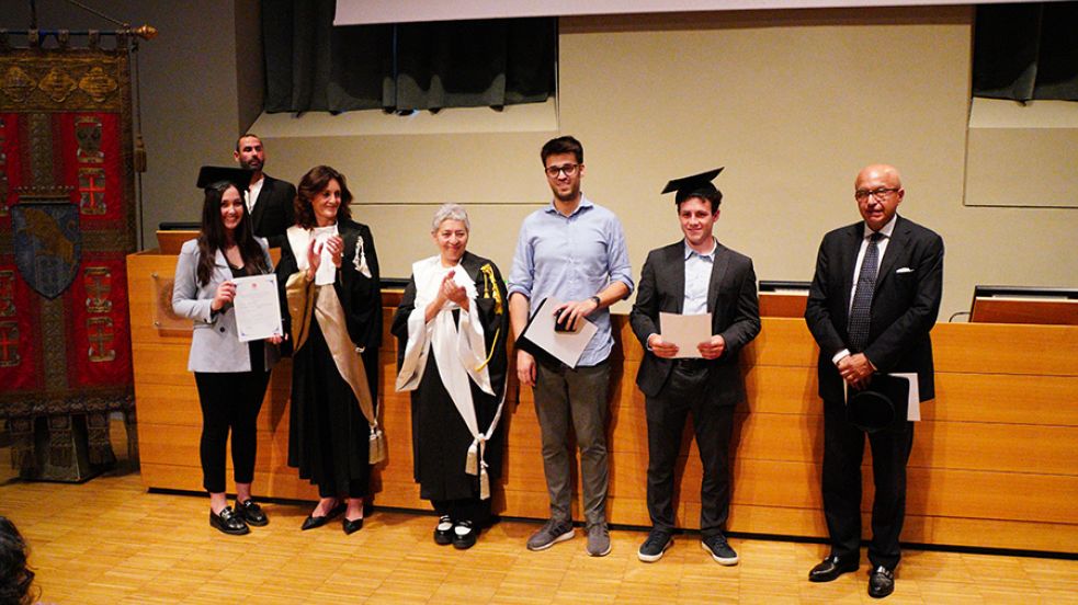 Tre persone con indosso il cappello da laureato, la prorettrice, una professoressa in toga e un professore posano di fronte al fotografo nell'aula magna della Cavallerizza in occasione della Festa della Conoscenza - Migliori Laureate e Laureati