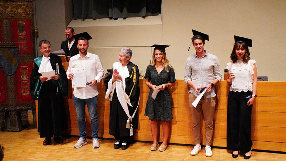 Quattro persone con indosso il cappello da laureato, la prorettrice e un professore in toga posano di fronte al fotografo nell'aula magna della Cavallerizza in occasione della Festa della Conoscenza - Migliori Laureate e Laureati