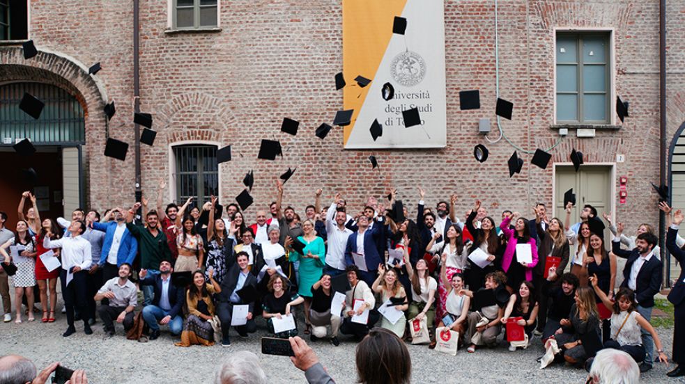 Gruppo di persone in posa davanti all'ingresso della Cavellerizza reale. Alcuni lanciano in aria dei cappelli da laureato