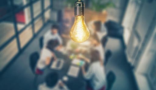 immagine di una lampadina accesa sopra a un tavolo con persone che lavorano