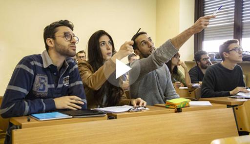Studenti in aula che indicano in direzione di uno schermo o lavagna 