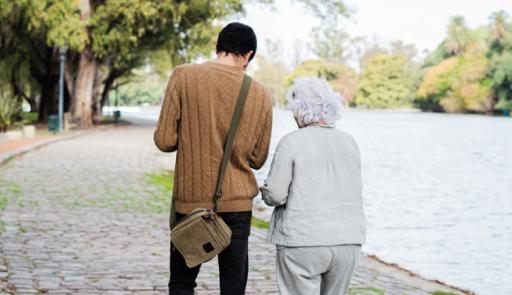 Due persone di schiena passeggiano all'aperto, sono un uomo giovane e una donna anziana