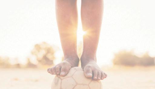 piedi di un bambino sopra un pallone da calcio durante il tramonto