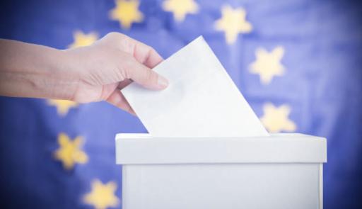 Mano con scheda elettorale in fase di voto, sullo sfondo bandiera dell'Europa