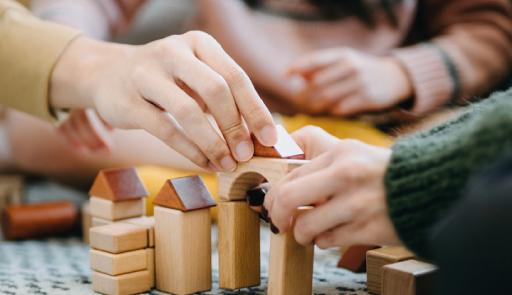 mani che stanno realizzando una piccola costruzione con pezzi di legno