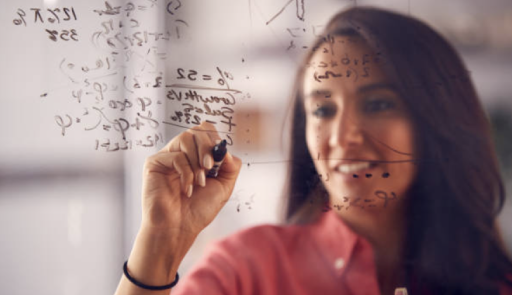 Fotografia che ritrae una donna con i capelli lunghi e scuri intenta a scrivere alla lavagna formule matematiche
