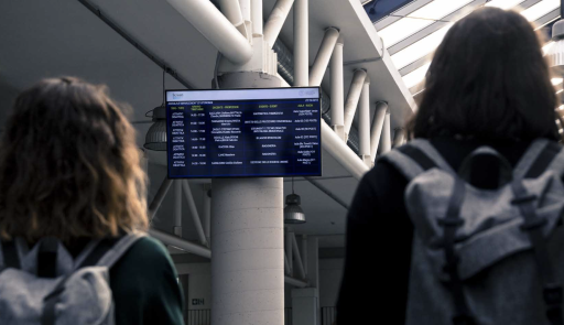 Immagine di due studentesse con zaini sulle spalle che guardano un monitor che contiene indicazioni sulle lezioni