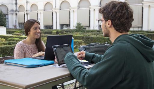 Studentessa e studente con computer seduti ad un tavolo di fronte l'uno all'altra