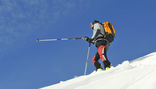 Sciatore con bastoncino e zaino in spalla che indica qualcosa con il bastoncino alzato della mano destra