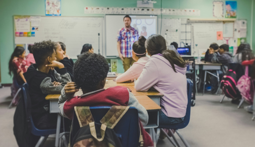 Svolgimento di una lezione in una classe media. L'insegnante è in piedi che spiega e alunni e alunne sono seduti e ascoltano