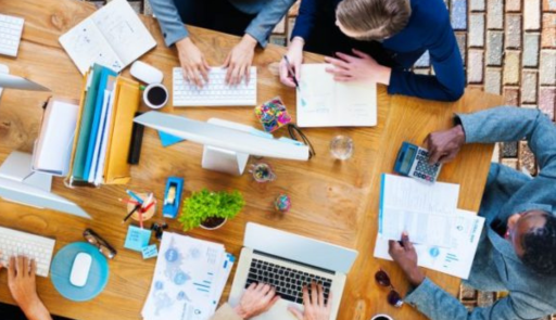 Immagine decorativa. Persone sedute attorno ad un tavolo di lavoro con pc, penne e quaderni
