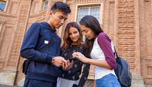 uno studente e due studentesse di vare nazionalità guardano un cellulare di fronte a Palazzo Carignano a Torino