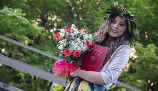 Studentessa laureata con mazzo di fiori e tesi tra le mani e la corona di alloro in testa