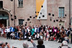 Gruppo di persone in posa davanti all'ingresso della Cavellerizza reale. Alcuni lanciano in aria dei cappelli da laureato
