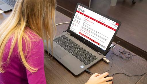 Studentessa seduta con un pc portatile e la mano sul mouse che effettua una ricerca sul portale di Ateneo