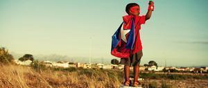 Bambino di colore con il mantello di Capitan America in un paesaggio africano