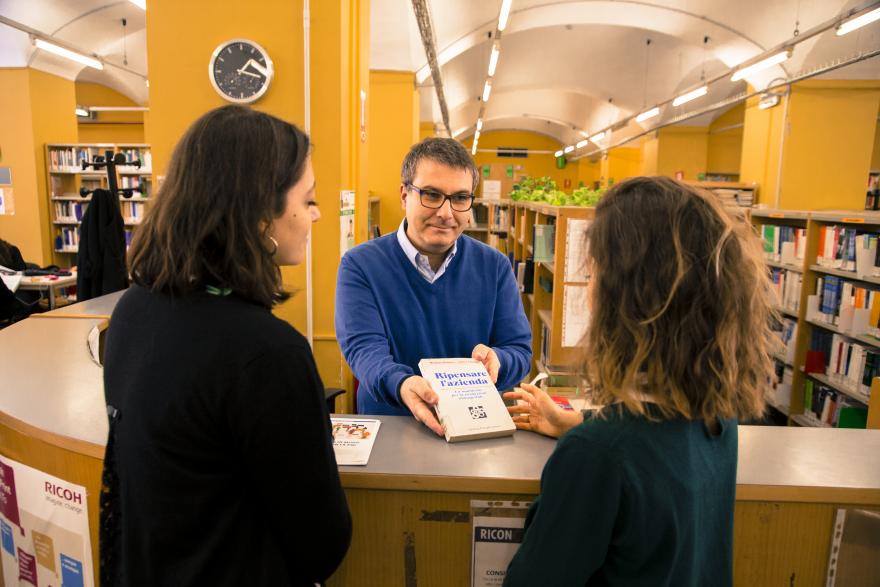 Bibliotecario che porge un libro a due studentesse