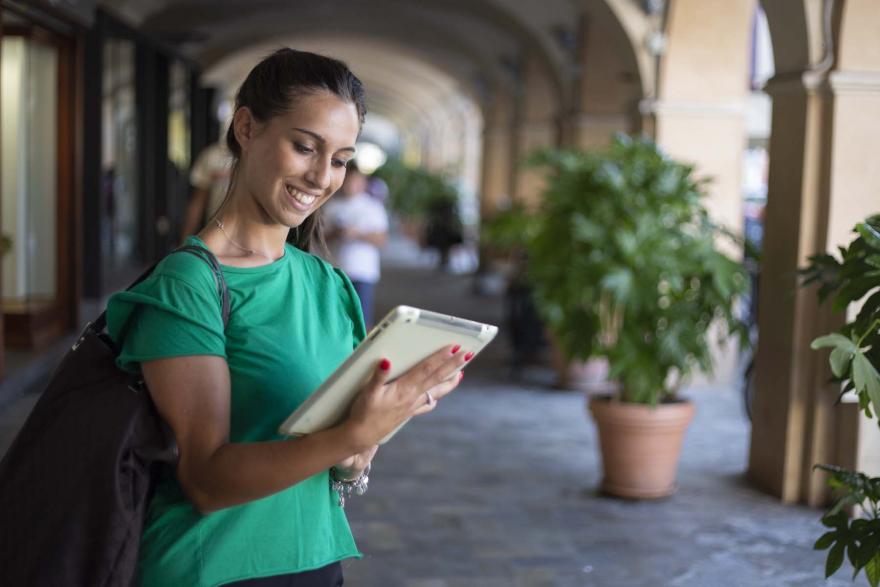 Una giovane donna consulta un tablet in una via cittadina