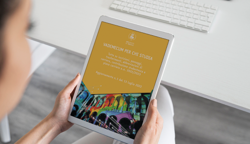 Scarica il vademecum per chi studia Ragazza tiene in mano un tablet che visualizza sul display la copertina del vademecum per chi studia