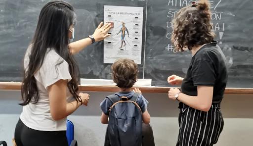 un bambino e due donne di spalle che guardano una lavagna