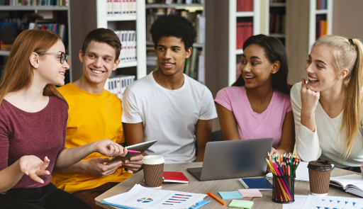 Gruppo di studenti che discutono seduti intorno ad un tavolo sul quale c'è un computer e un astuccio con delle matite. Uno degli studenti regge un tablet in mano