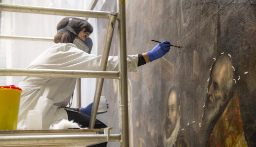 restauratrice con camice e maschera protettiva nell'atto di restaurare un quadro 