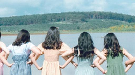 Gruppo di bambine a braccetto, fotografate di schiena, di sfondo uno specchio d'acqua e delle colline