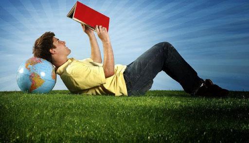 Un uomo legge un libro in un prato con la testa appoggiata al mappamondo